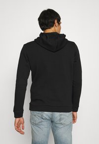 Sudadera negra con bolsillo canguro en el frente, capucha con cordones y puños de canalé, combinada con jeans de mezclilla azul claro. Textura de tela suave visible.