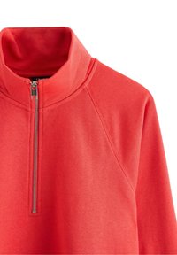 Felpa rossa con cerniera e collo alto, caratterizzata da maniche raglan e texture liscia. La robusta cerniera argentata sul collo aggiunge un dettaglio.