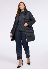 Svart vadderad jacka med hög krage, dragkedja och gulddetaljer. Bärs över en mörk tröja och mörka denimfasoner med strass.