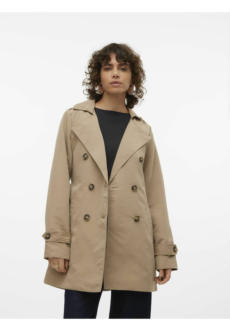 Beige trenchcoat med dubbelknäppt design, breda slag och stora knappar. Slät textur och avslappnad passform som når till mitten av låret.