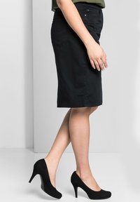 Falda negra hasta la rodilla con corte recto, hecha de tela suave, que cuenta con dos bolsillos laterales y cierre frontal con botones. Un par de tacones altos negros.