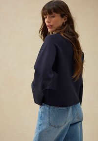 Marineblauwe trui met een relaxte pasvorm en verlaagde schouders, gecombineerd met lichtblauwe high-waisted jeans. Soepele textuur en minimale ontwerpdetails.