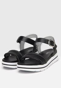 Sandalias de cuero negro con dos correas anchas, tachuelas decorativas y cierre de hebilla. Presentan una suela acolchada blanca con detalles en negro.