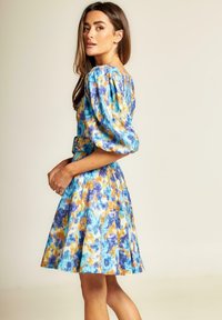 Blumenmusterkleid in Blau, Gelb und Weiß. Mit Puffärmeln, tailliertem Schnitt und ausgestellt Rock, aus leichtem Stoff gefertigt.