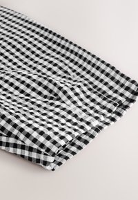 Schwarz-weiß kariertes Stoffstück, ordentlich gefaltet. Die Textur wirkt weich und gewebt und zeigt ein klassisches Vichymuster mit gleichmäßigen Quadraten.