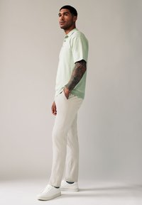 Polo a maniche corte verde menta, pantaloni bianchi slim-fit e sneakers bianche. Il tessuto appare liscio con una leggera trama.