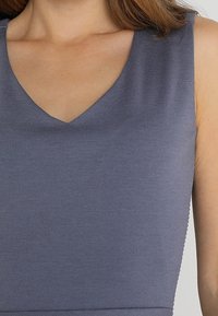 Ärmelloses V-Ausschnitt-Top aus weichem grauen Stoff, das eine glatte Textur und ein tailliertes Design aufweist, das eine klare Silhouette ohne Verzierungen hervorhebt.