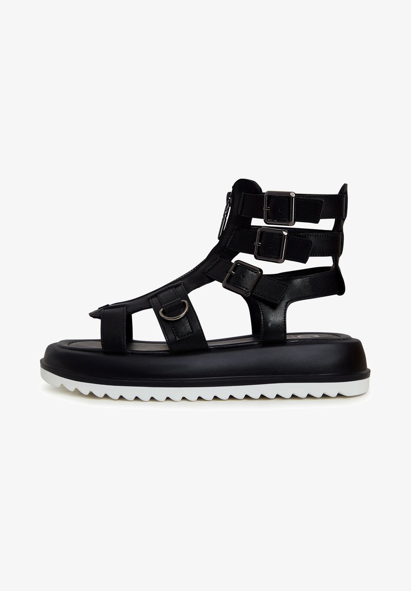 Sorte gladiator sandaler med flere stropper og spænder, lynlås-lukning og en tyk hvid zigzag sål. Glat læderoverflade.