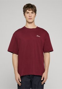 Burgundijas krāsas t-krekls no kokvilnas ar apaļu kakla izgriezumu un īsām piedurknēm. Uz krūtīm ir neliels izšūts logo. Brīva piegriezte.