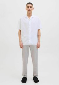 Chemise blanche à manches courtes, col avec boutons, accompagnée d'un pantalon gris clair et de chaussures noires à enfiler. Design simple et décontracté.