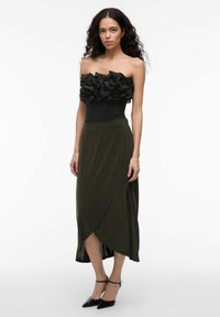 Czarny bezramkowy top z warstwowymi falbanami; oliwkowa, zwiewna spódnica o konstrukcji kopertowej; dopełniona czarnymi szpilkami z długim noskiem.