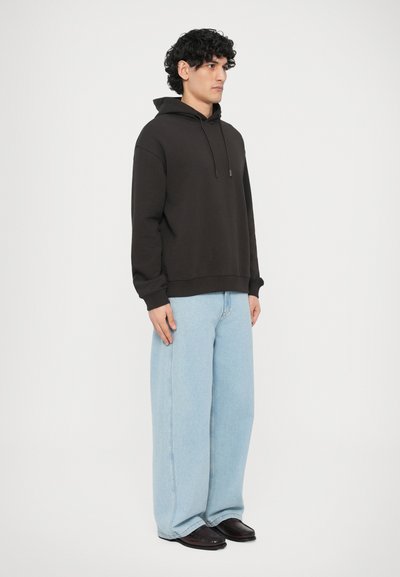 Μαύρο φούτερ με κουκούλα, μπροστινή τσέπη καγκουρό και κορδόνια. Συνδυασμένο με ανοιχτό μπλε φαρδιά τζιν παντελόνια και μαύρα παπούτσια. Ομαλή υφή.