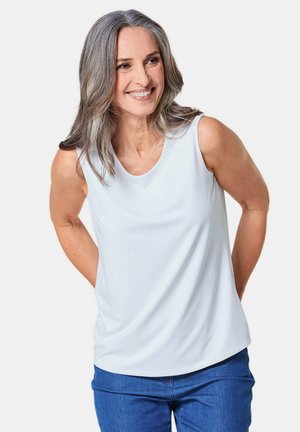 Mouwloos wit topje van gladde stof, met een ronde halslijn en een relaxed fit, gecombineerd met blauwe jeans.