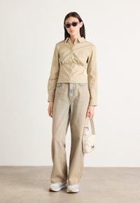 Béžová upnutá košile s button-down přední částí a nařaseným pasem, v kombinaci s světlými džíny. Doplněna bílými teniskami a malou taškou.