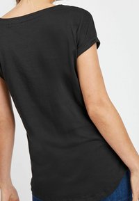 Czarny t-shirt z krótkim rękawem o luźnym kroju, wykonany z gładkiej bawełny, z okrągłym dekoltem, podwiniętymi mankietami i zaokrąglonym dołem.