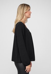 Black long-sleeve top with a loose fit, textured fabric, and a rounded neckline. Sleeves feature elastic cuffs. Designed for comfort.