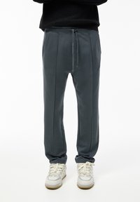 Grå sweatpants med elastisk midjeband och justerbar dragsko, med sidfickor och vertikala sömmar, parat med vita sneakers.