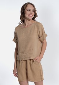Top in lino beige con maniche corte arrotolate e vestibilità rilassata, abbinato a pantaloni corti in lino beige con tasche laterali.