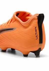 Oranje voetbalschoen met een gestructureerde synthetische bovenkant, zwarte accenten en een prominent "ULTRA" logo aan de zijkant. Beschikt over gemodelleerde zwarte noppen.