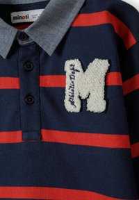 Granatowa i czerwona koszulka polo w paski z dżinsowym kołnierzykiem, z teksturowaną białą aplikacją "M" oraz trzema czarnymi guzikami na listwie.