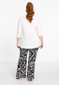Witte langvolledige top met omgeslagen mouwen, gecombineerd met zwart-witte wijde broeken met een patroon van bloemen. Soepele stoftextuur.