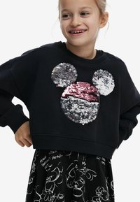 Schwarzes, kurzes Sweatshirt mit einem Pailletten-Mickey-Mouse-Design in Silber, Grau und Pink. Kombiniert mit einem schwarzen Rock mit weißen Grafiken.
