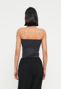 Haut bustier gris foncé en tissu lisse, avec une coupe ajustée et un motif texturé subtil au dos. Associé à un pantalon noir ample.
