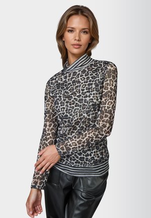 Woman with light brown hair wearing a sheer long-sleeve leopard print top with striped collar and cuffs, paired with black leather pants.