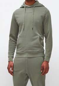 Felpa verde oliva con cappuccio regolabile, tasca a marsupio e polsini a coste. Realizzata in morbido tessuto misto cotone. Stampa di testo sul petto.