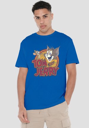 Young man wearing a blue T-shirt with vintage-style Tom and Jerry cartoon faces and bold red text on the front.