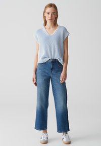 Striped blue and white knit top with short sleeves, paired with high-waisted, straight-leg blue jeans and white sneakers with gum soles.