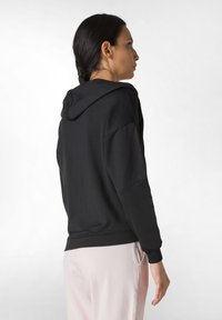 Sudadera negra con capucha, de mangas largas, puños acanalados y corte relajado. Tejido suave y diseño minimalista, combinada con pantalones rosa claro.
