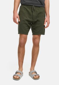 Oliven grønne shorts med strukturet design, elastisk talje og snor. Kombinert med grå sandaler med justerbare spenner.