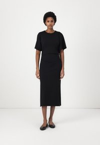 Black midi dress with short puff sleeves, a fitted bodice, and a straight skirt. Smooth fabric with a slight sheen. Paired with black flats.