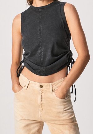 Haut court sans manches noir avec un col rond, doté de cordons de serrage sur les côtés et de coutures contrastantes. Associé à un pantalon taille haute de couleur claire.