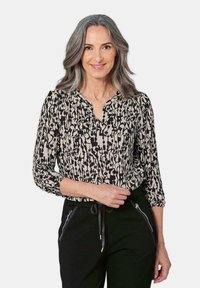 Zwarte en beige abstracte patroon blouse met een henleyhalslijn en driekwart mouwen, gemaakt van lichtgewicht stof. Gecombineerd met zwarte broeken.