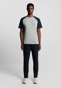 Grå t-shirt med marineblå ærmer og lys trim, parret med marineblå joggers og beige sneakers. Enkel design, afslappet pasform og komfortable materialer.