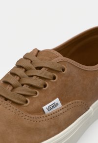 Bruine suède veterschoen met een ronde neus, tonale veters, witte rubberen zool en een klein Vans-logo label aan de zijkant.