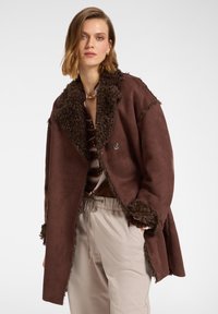 Manteau en suédine marron avec un col et des poignets texturés et duveteux. Doté d'une fermeture à un bouton, d'une coupe loose et d'un design mi-long.