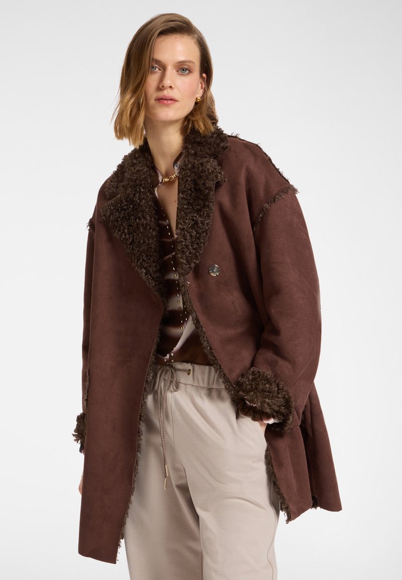 Manteau en suédine marron avec un col et des poignets texturés et duveteux. Doté d'une fermeture à un bouton, d'une coupe loose et d'un design mi-long.