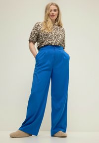 Een kort mouwenshirt met luipaardprint, gecombineerd met blauwe wijde broeken met een hoge taille en zijzakken. Zachte beige slippers maken de look compleet.