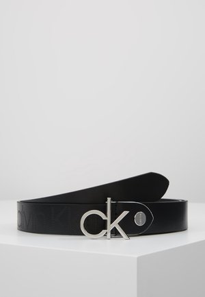 Schwarzer Ledergürtel auf weißem Untergrund aufgewickelt, mit silberner "ck"-Schnalle und eingeprägtem "Calvin Klein"-Logo entlang des Riemens.