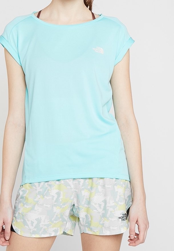 T-shirt de sport bleu clair à manches courtes avec un col rond et un logo. Associé à un short gris avec un motif abstrait coloré.