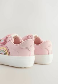 Baskets en faux cuir rose avec une finition texturée, ornées d'un design arc-en-ciel sur le côté et de semelles en caoutchouc blanches. Fermeture velcro.
