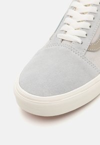Sneakers en daim gris clair avec une finition texturée, dotées de lacets plats blancs, d'une semelle en caoutchouc crème et de subtils détails de couture sur les côtés.