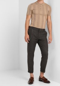 Beige polo shirt met korte mouwen en verticale strepen, gecombineerd met donkergrijze afgeknotte broek met een zijrits en bruine instappers.