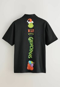 Musta lyhythihainen paita, jossa etupuolella grafiikka Grinchistä joulupukin hatun kanssa, teksti "12 DAYS GRINCHMAS" ja värikkäitä lahjoja punaisessa laukussa.
