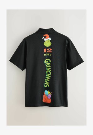 Zwarte t-shirt met korte mouwen, afgebeeld met Grinch-graphics, waaronder "12 DAGEN" en "GRINCHMAS" in kleurrijke tekst, met onderaan een rode geschenktas.