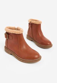 Braune Lederstiefeletten mit einem flauschigen beigen Kragen, seitlichem Reißverschluss und einer kleinen seitlichen Schnalle. Strukturiertes Obermaterial und flache Sohle.