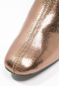 Chaussure pointue en or rose métallique avec une texture craquelée, présentant une surface lisse et des coutures contrastantes le long du centre.